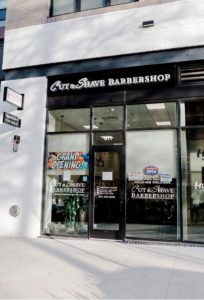 storefront for cut and shave barbershop with grand opening sign up in the window